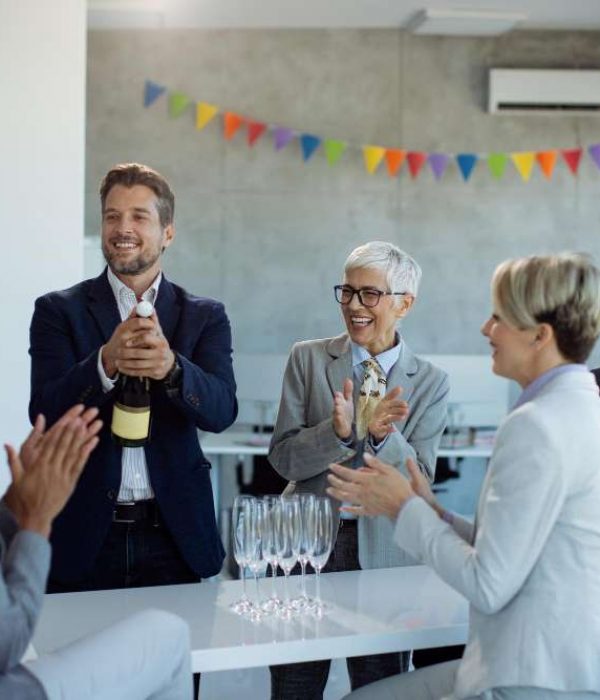 happy-business-people-opening-bottle-champagne-while-celebrating-office-party